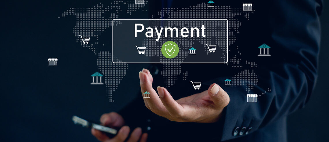 A hand holding a smartphone is in focus against a digital world map background. The word Payment and various icons, like shopping carts and bank buildings, convey a theme of global online transactions