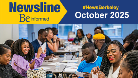 Newsline. Be informed. A diverse group of people engaged in a discussion around a table, with papers and a vibrant classroom setting in the background.